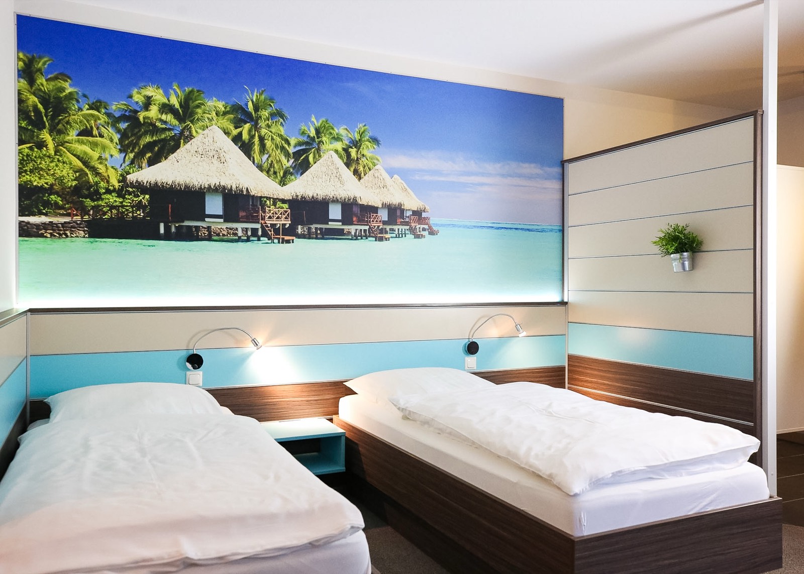 Themenzimmer Südsee im Hotel Ripken mit beleuchtetem Wandbild von Wasserbungalows über dem Bett